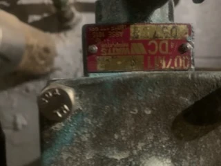 Pink Watts backflow preventer serial tag riveted to a weathered brass valve body