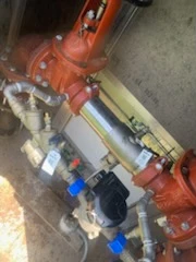 Large commercial backflow assembly with orange grooved fittings and copper piping in a mechanical room