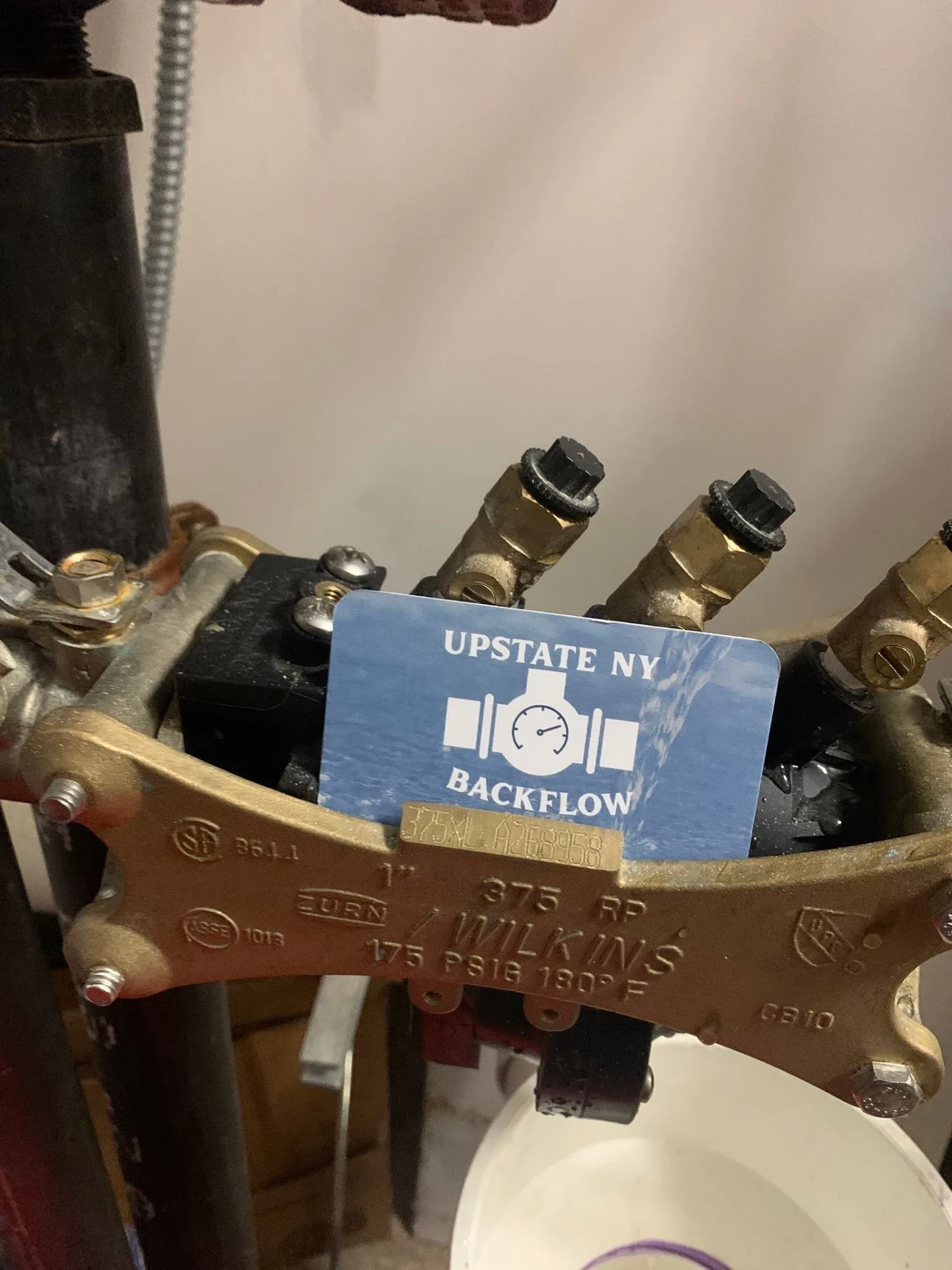 Blue Upstate NY Backflow business card with water logo sitting on a Zurn Wilkins 375 RP assembly