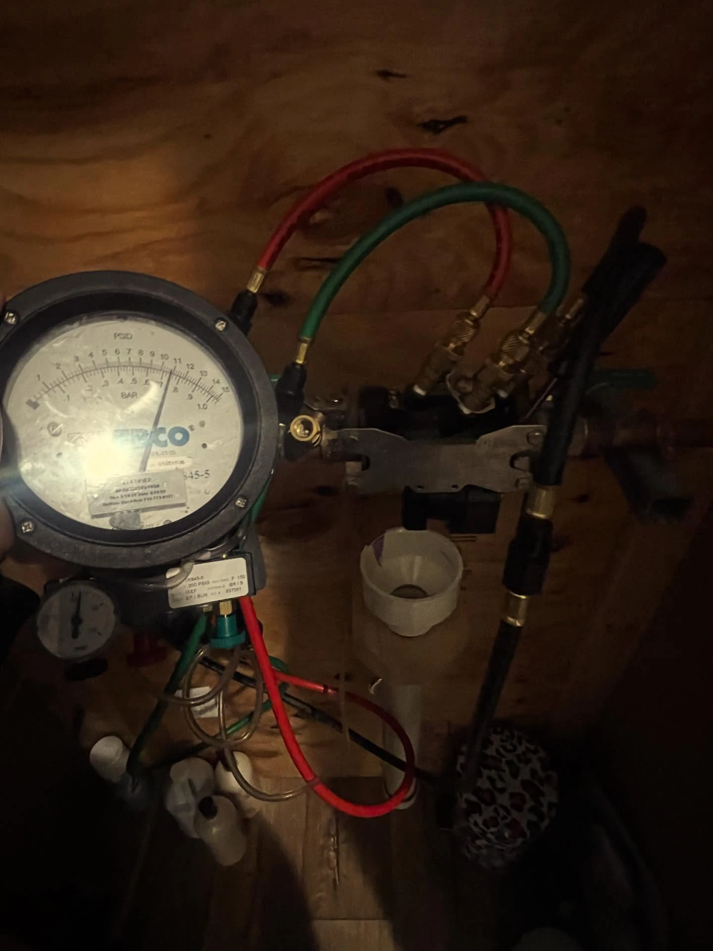 Technician holding a Febco backflow test gauge with hoses connected in a dimly lit basement