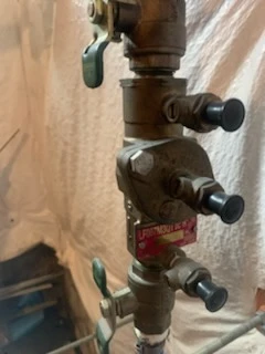 Bronze reduced pressure backflow assembly with black capped test cocks and a green shutoff handle on a residential water service