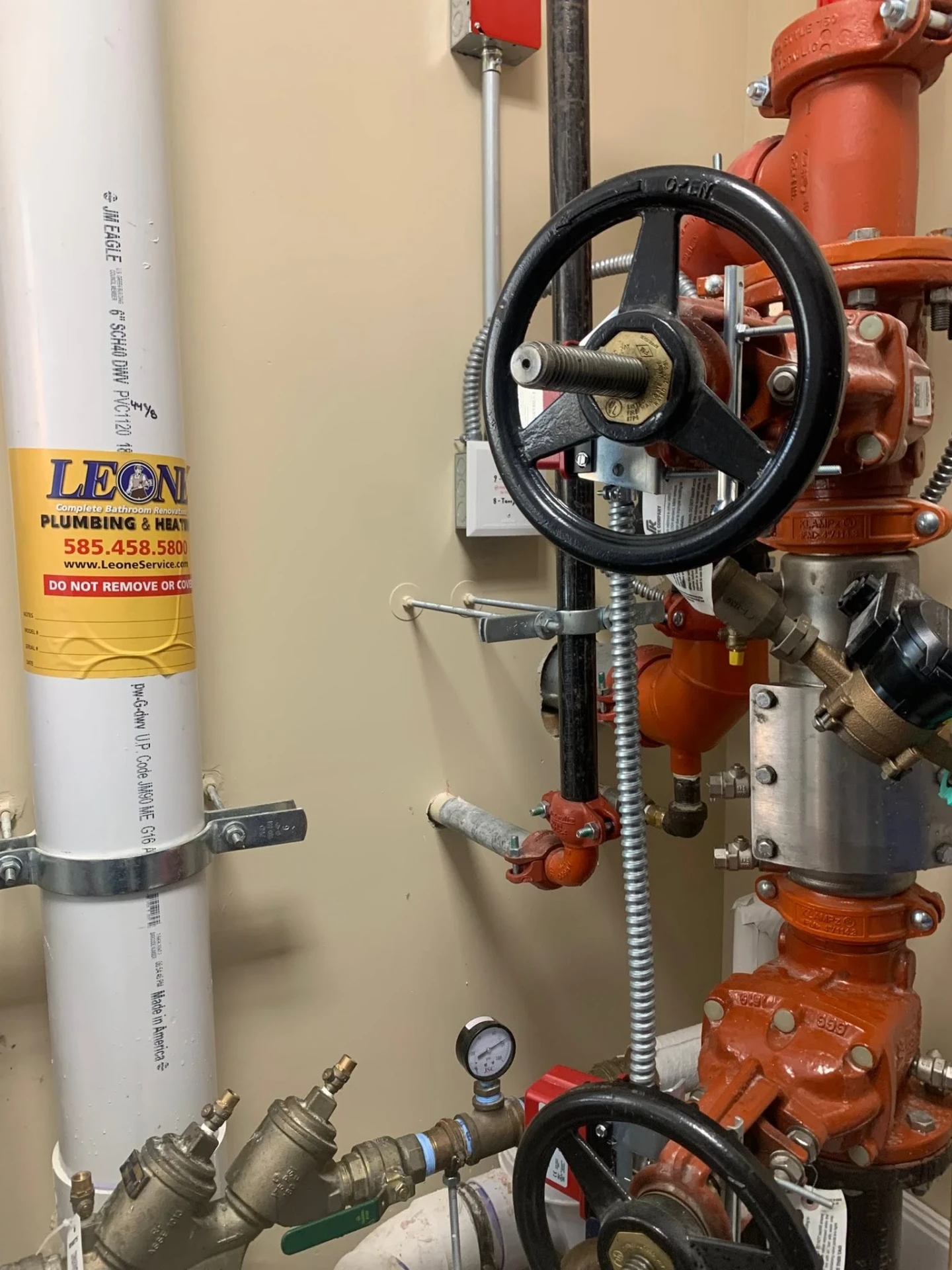 Red fire sprinkler riser with backflow assembly, tamper switch, and white PVC drain line in a commercial mechanical room