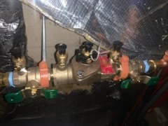 Brass double check backflow assembly with red and blue handled shutoff valves in a basement