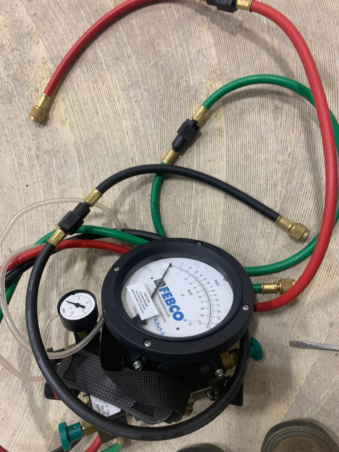 Febco TK845 backflow test kit with red, green, and black hoses laid out on a workbench